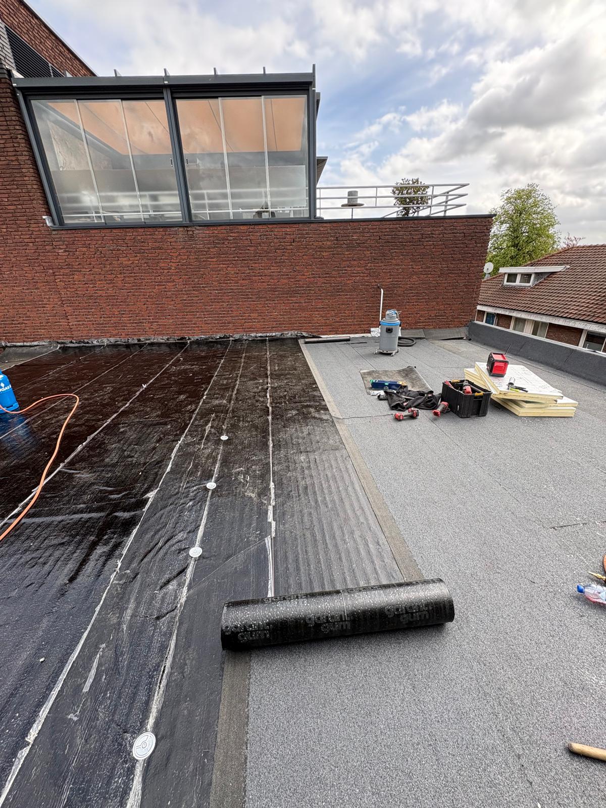 Nieuwe rol bitumen wordt uitgerold op een plat dak in Oosterhout