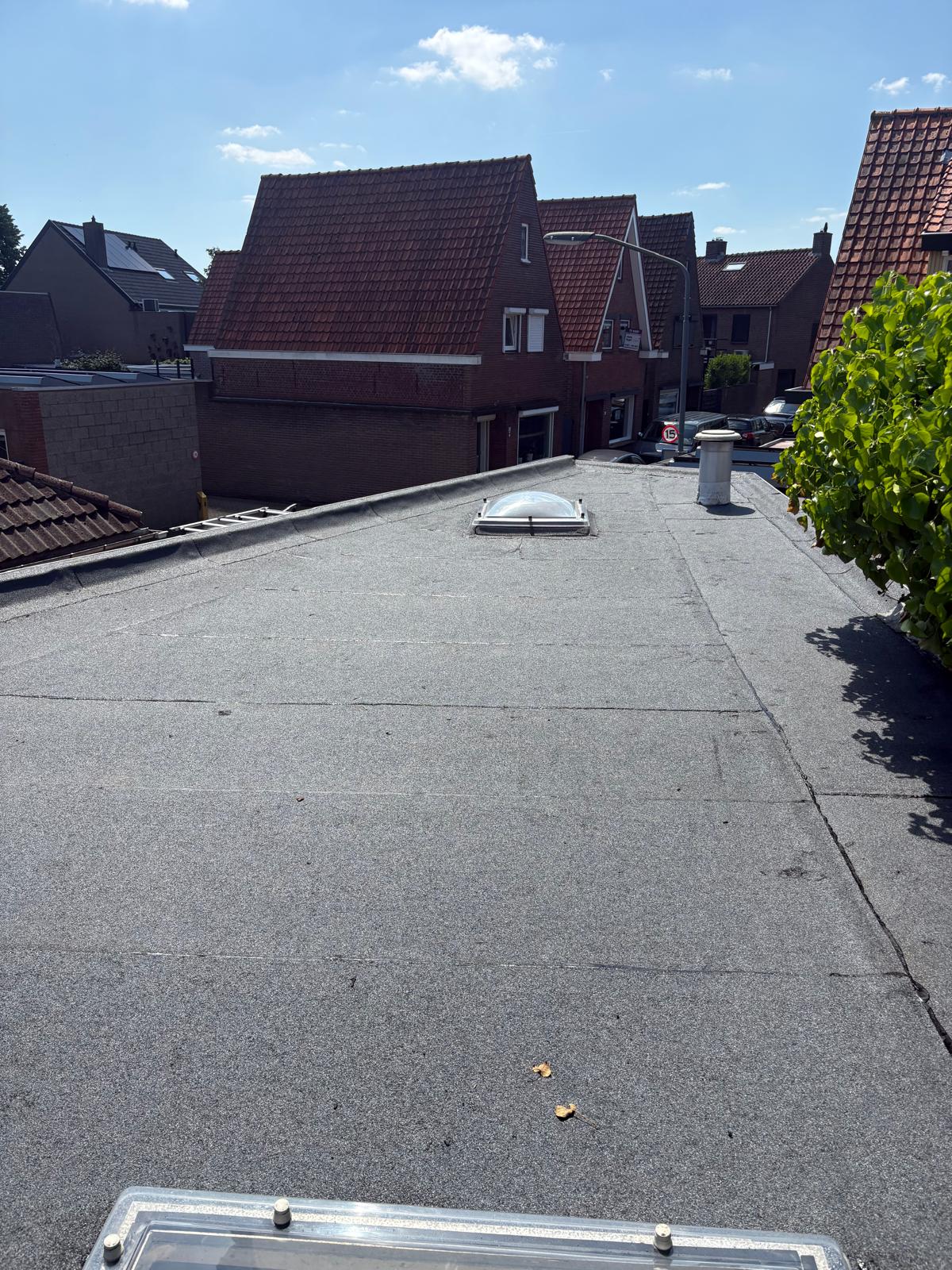 Nieuw bitumen dak met twee lichtkoepels tussen woningen met pannendaken