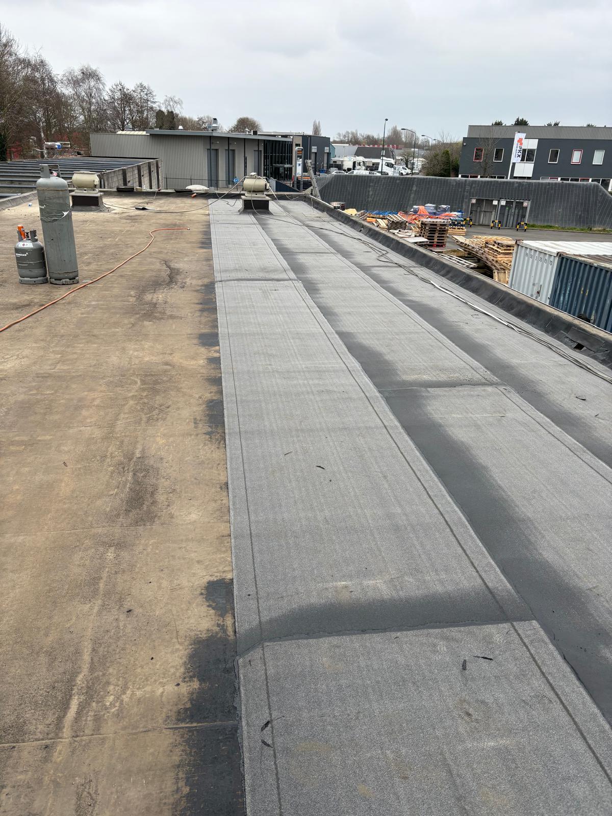 Bedrijfsdak met een nieuw aangebrachte baan bitumen en gasflessen voor het branden